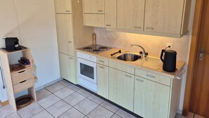 A compact kitchen with light wood cabinets, a stainless steel sink, a stove, and a small shelf with kitchen appliances. - Cozy vacation apartment - nature & relaxation (Aeschi bei Spiez)