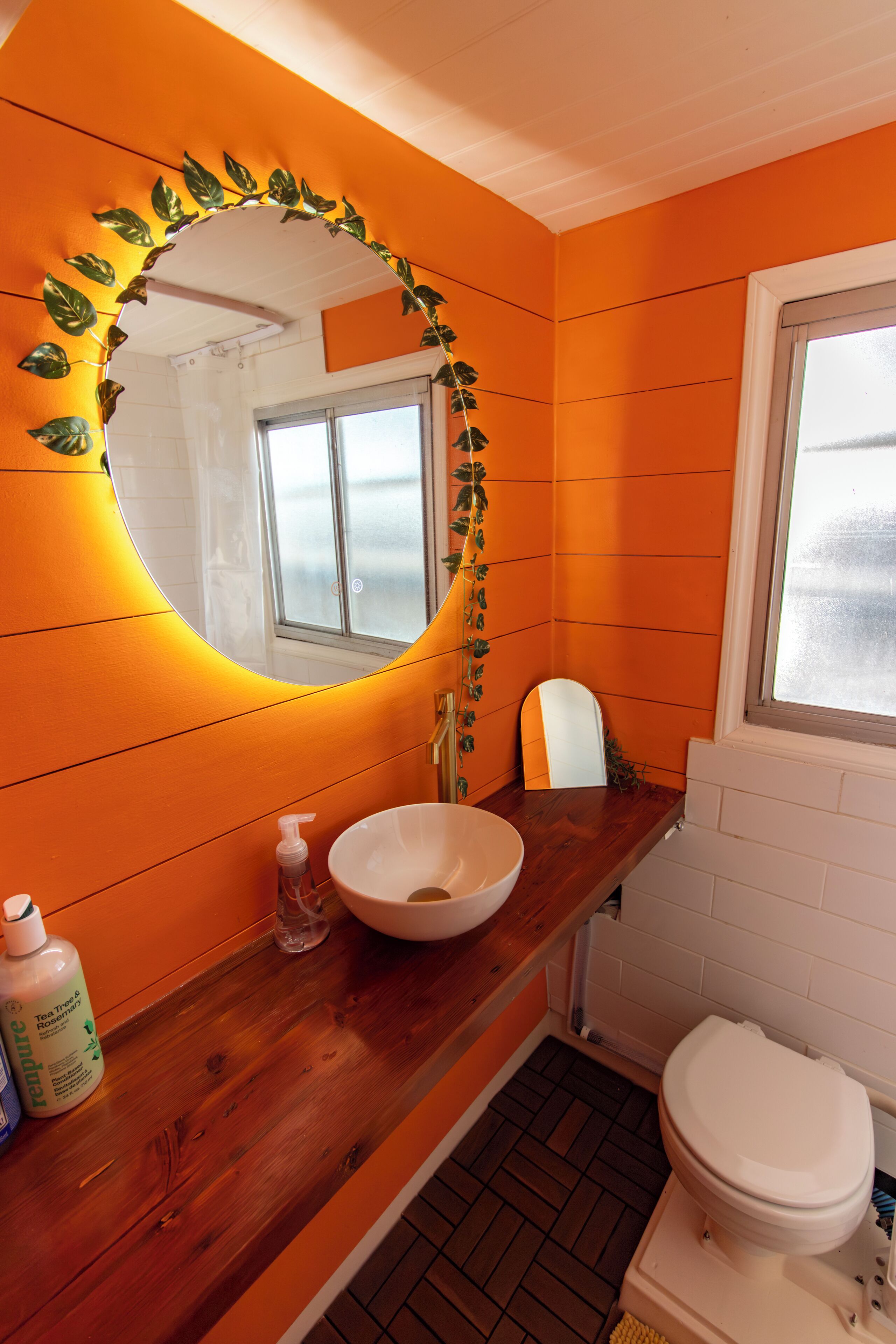 Ett badrum med en orange vägg, ett handfat i trä, en vit tvättställ och en toalett.