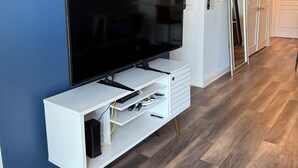 Una sala moderna con un televisor de pantalla plana sobre un mueble blanco, piso de madera y una pared azul de acento.