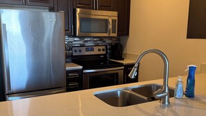 Una cocina con un refrigerador de acero inoxidable, un microondas, un horno y un lavamanos con una llave moderna.