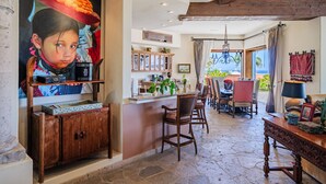 A spacious dining area with a view of the sea, a kitchen with wooden cabinets, and a large painting on the wall.