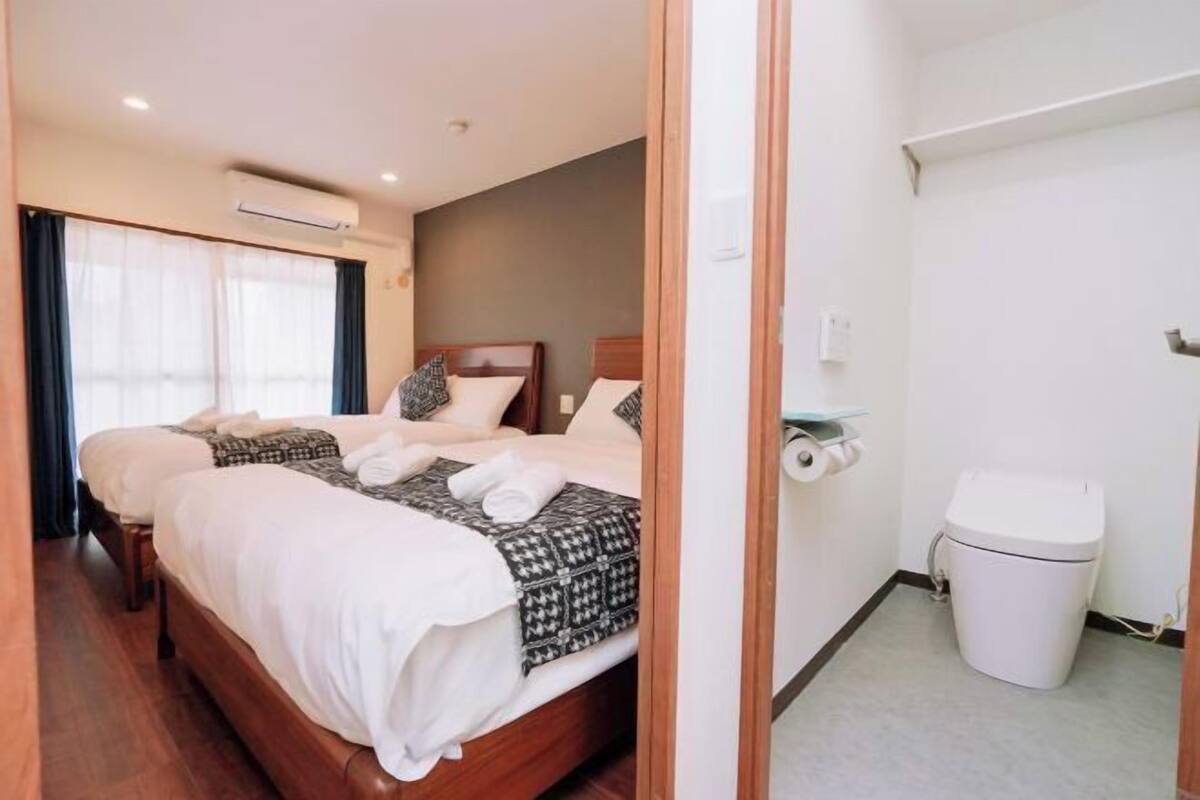 Habitación de hotel con cama doble, mesita de noche, cubo de basura y ventana con cortinas.