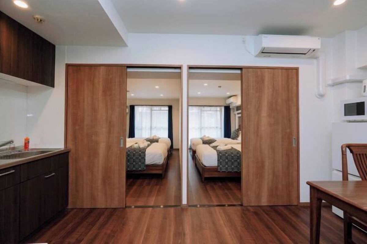 Una habitación con piso de madera, una cama con colcha estampada, un armario de madera, una mesita y un microondas.