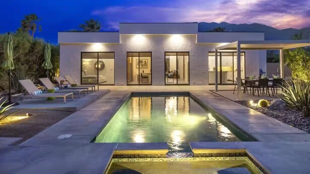 Een modern huis met een zwembad, terras en een berg op de achtergrond.