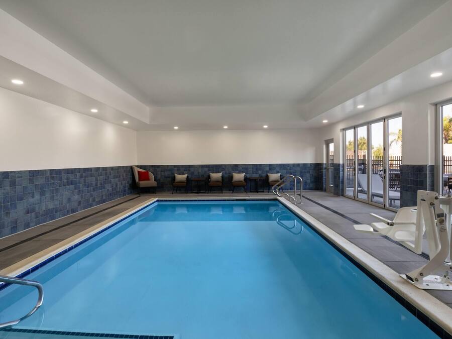 A swimming pool with a blue tiled border, a seating area with chairs and a sofa, and a glass door leading outside.