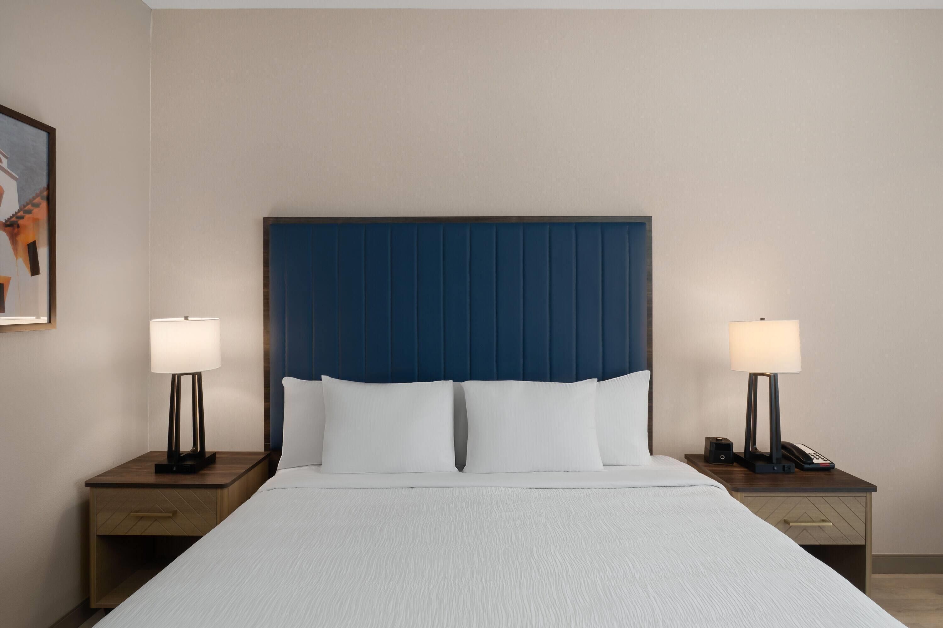 A hotel room with a large bed, two bedside tables with lamps, and a headboard.