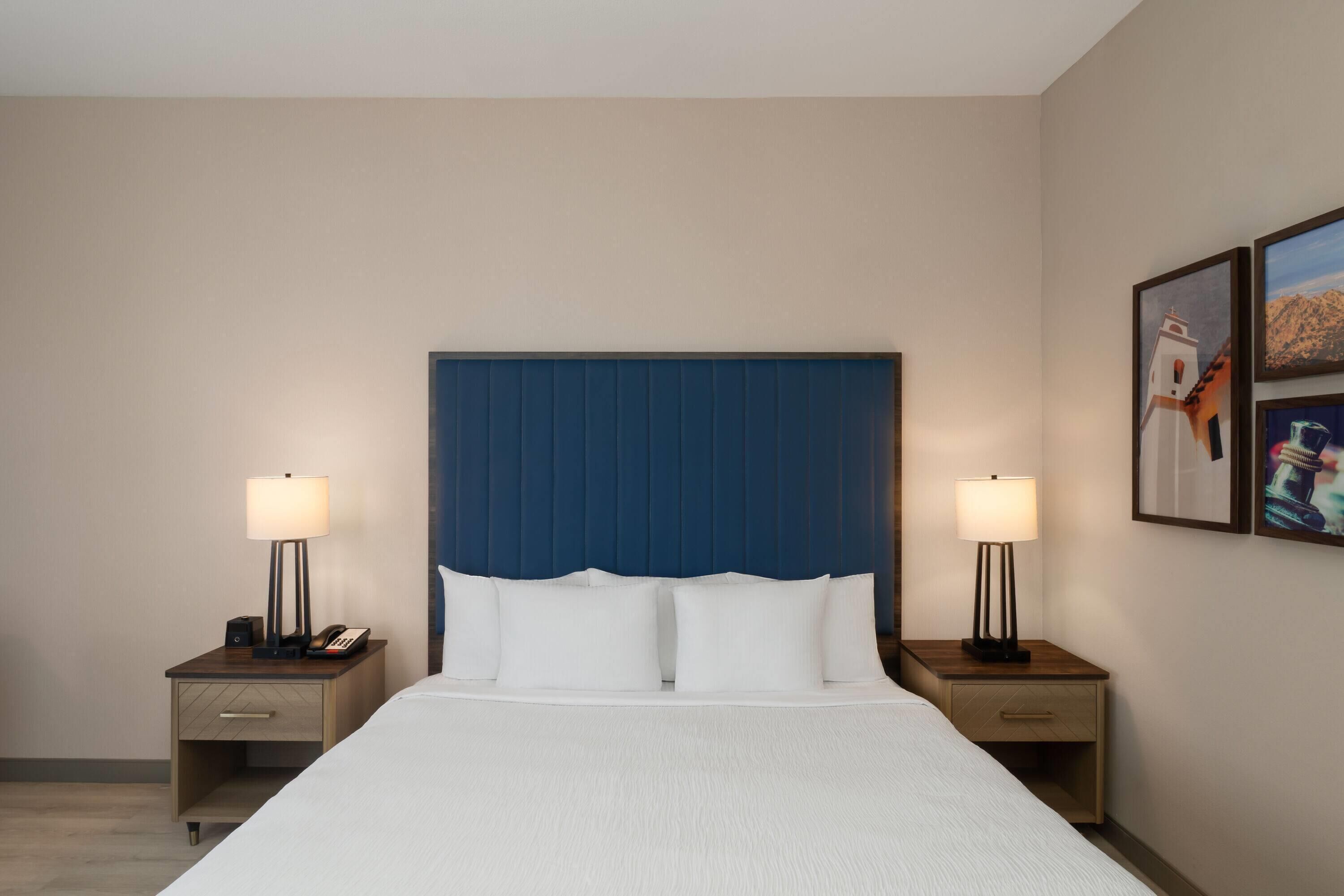 A hotel room with a large bed, two bedside tables with lamps, a telephone, and two framed pictures on the wall.