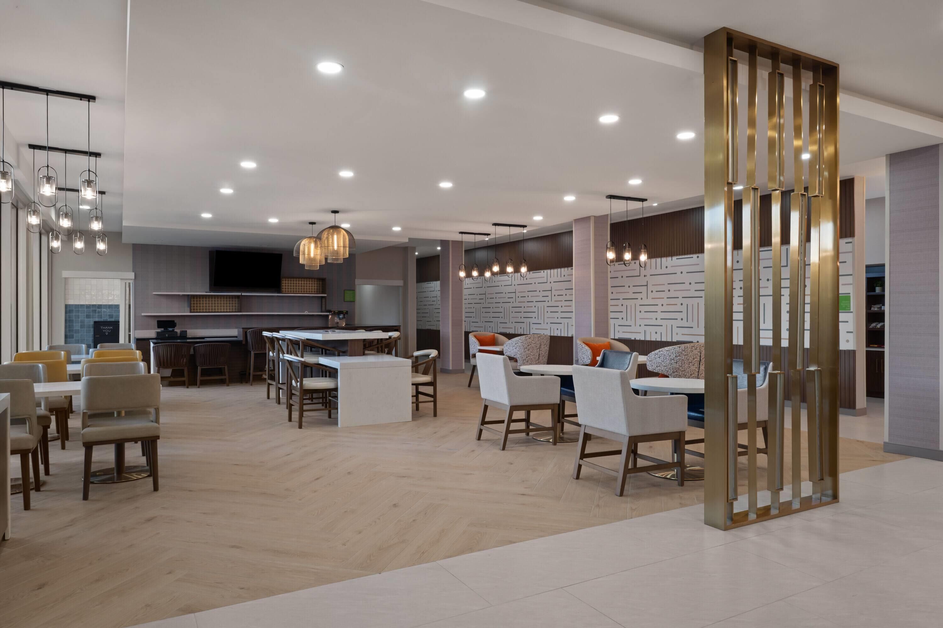 Un interior moderno con un área de comedor central, varios arreglos de asientos y una cocina al fondo.