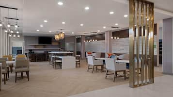 Un interior moderno con un área de comedor central, varios arreglos de asientos y una cocina al fondo.