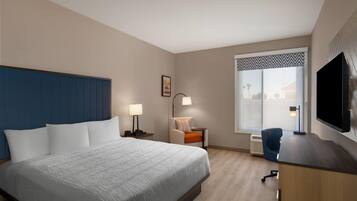 A hotel room with a large bed, a desk with a flat-screen TV, a chair, a desk lamp, and a window with a view.