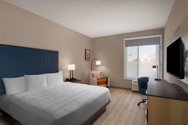 Une chambre d’hôtel avec un grand lit, un bureau doté d’un téléviseur à écran plat, une chaise, une lampe de bureau et une fenêtre donnant sur un paysage agréable.