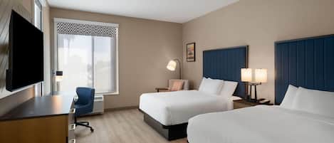A hotel room with two beds, a desk, a chair, a TV, and a window with a view.