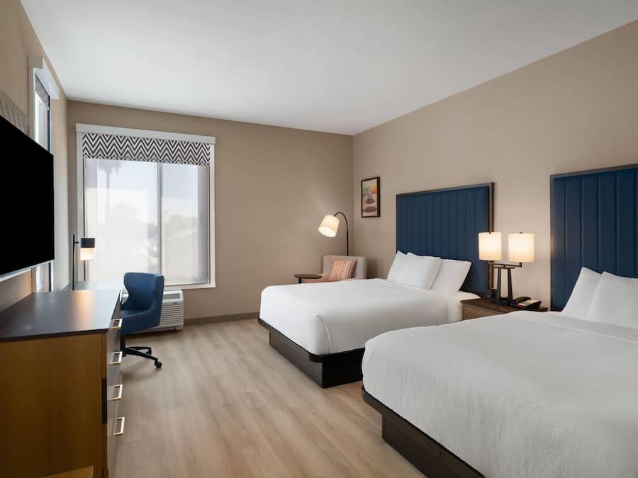 Habitación de hotel con dos camas, un escritorio, una silla, un televisor y ventana con vistas.