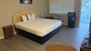 A hotel room with a bed, a small bedside table, a heater, a TV, and a view of the outside. - Travelodge By Wyndham Susanville (Susanville)