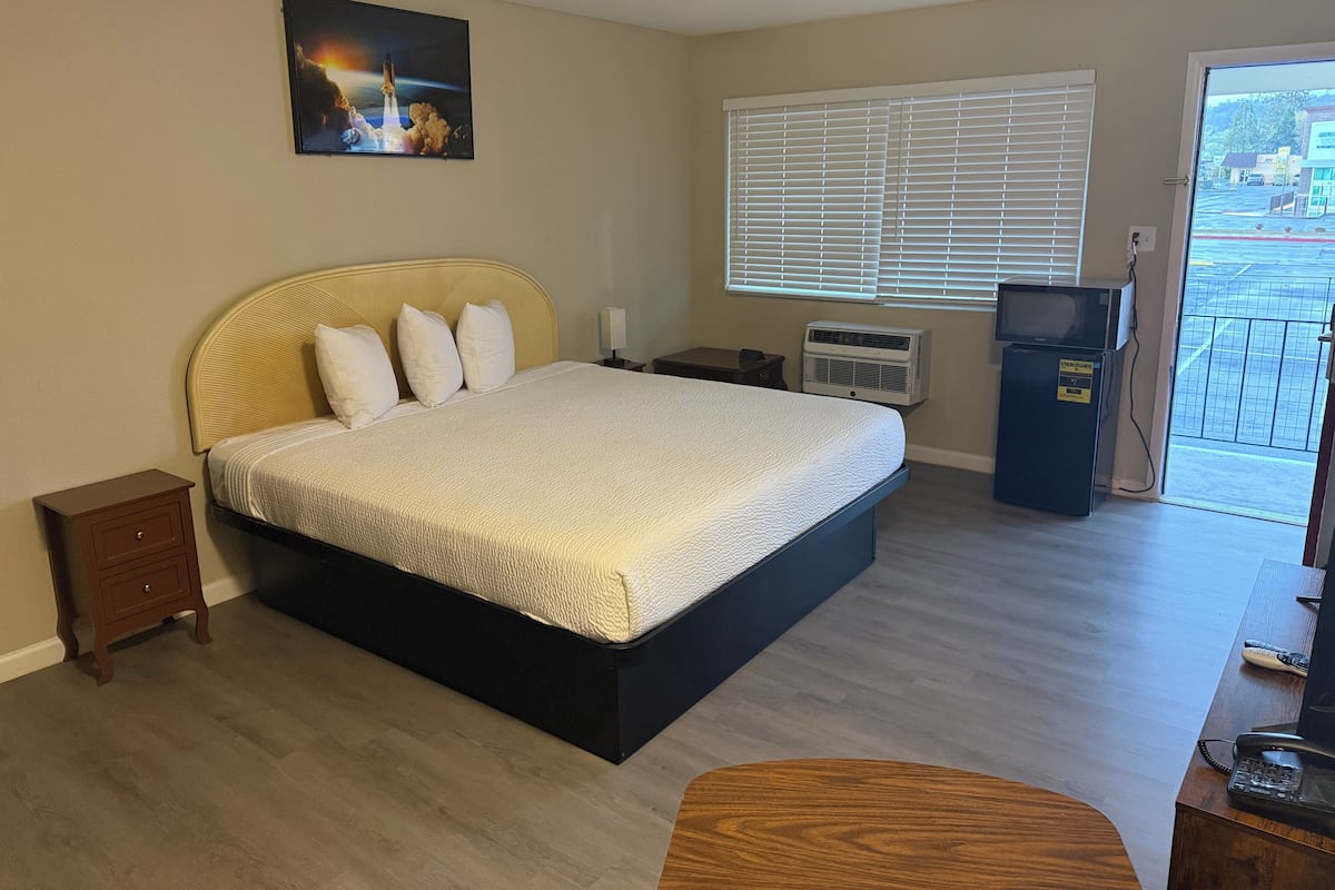 Habitación de hotel con cama, mesita de noche, calentador, televisor y vistas al exterior.