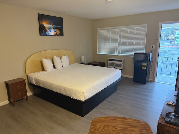 A hotel room with a bed, a small bedside table, a heater, a TV, and a view of the outside. - Travelodge By Wyndham Susanville (Susanville)
