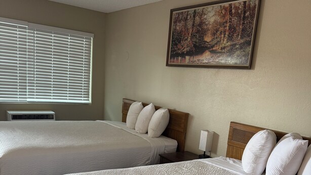 A hotel room with two beds, a painting on the wall, and a window with blinds. - Travelodge By Wyndham Susanville (Susanville)