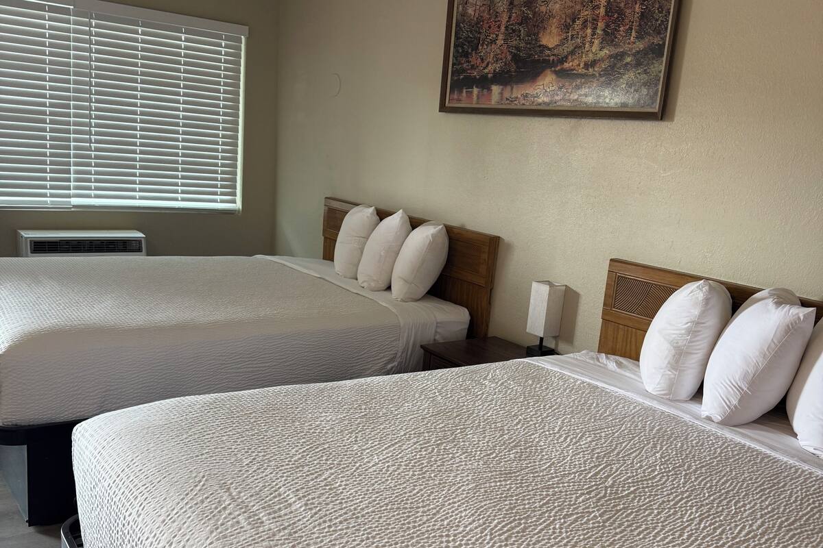 Habitación de hotel con dos camas, un cuadro en la pared y una ventana con persianas.