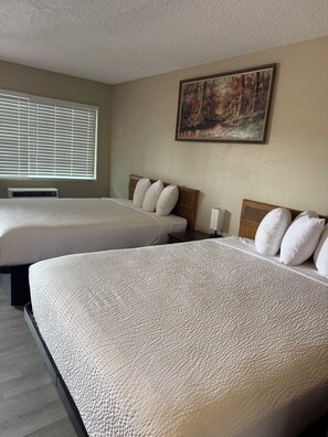 A hotel room with two beds, a painting on the wall, and a window with blinds. - Travelodge By Wyndham Susanville (Susanville)