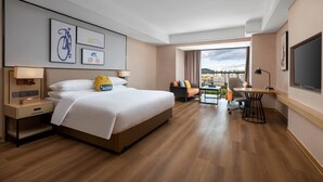 A hotel room with a large bed, a desk, a chair, and a view of the city.