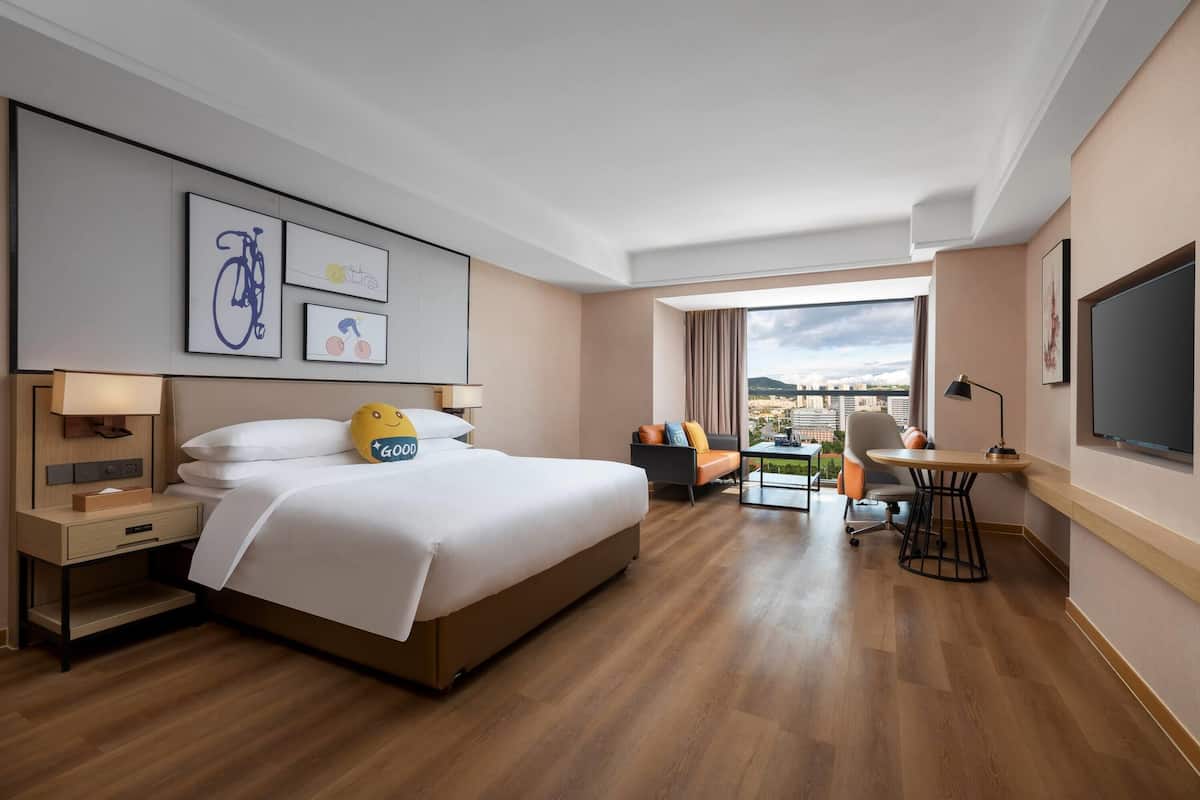 A hotel room with a large bed, a desk, a chair, and a view of the city.