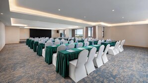 A conference room with rows of tables, white chairs, and green tablecloths.