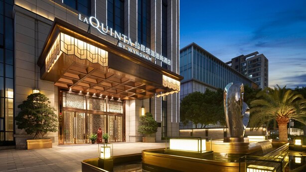Een hotelentree met een moderne gevel, een waterpartij en een goed verlicht buitengebied.