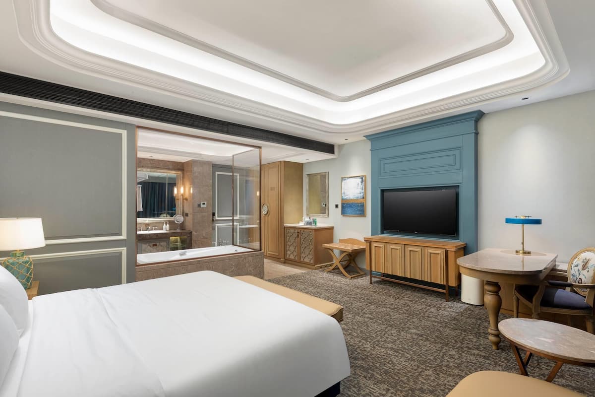 A hotel room with a large bed, a TV, a desk, and a bathroom with a bathtub and mirror.