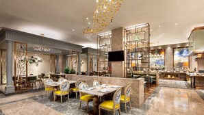 Een ruim restaurant met marmeren vloer, gele stoelen en een moderne kroonluchter.