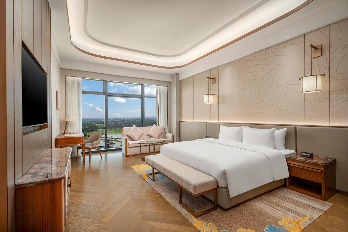 Una habitación de hotel moderna con una cama grande, un escritorio, un sofá y un televisor.