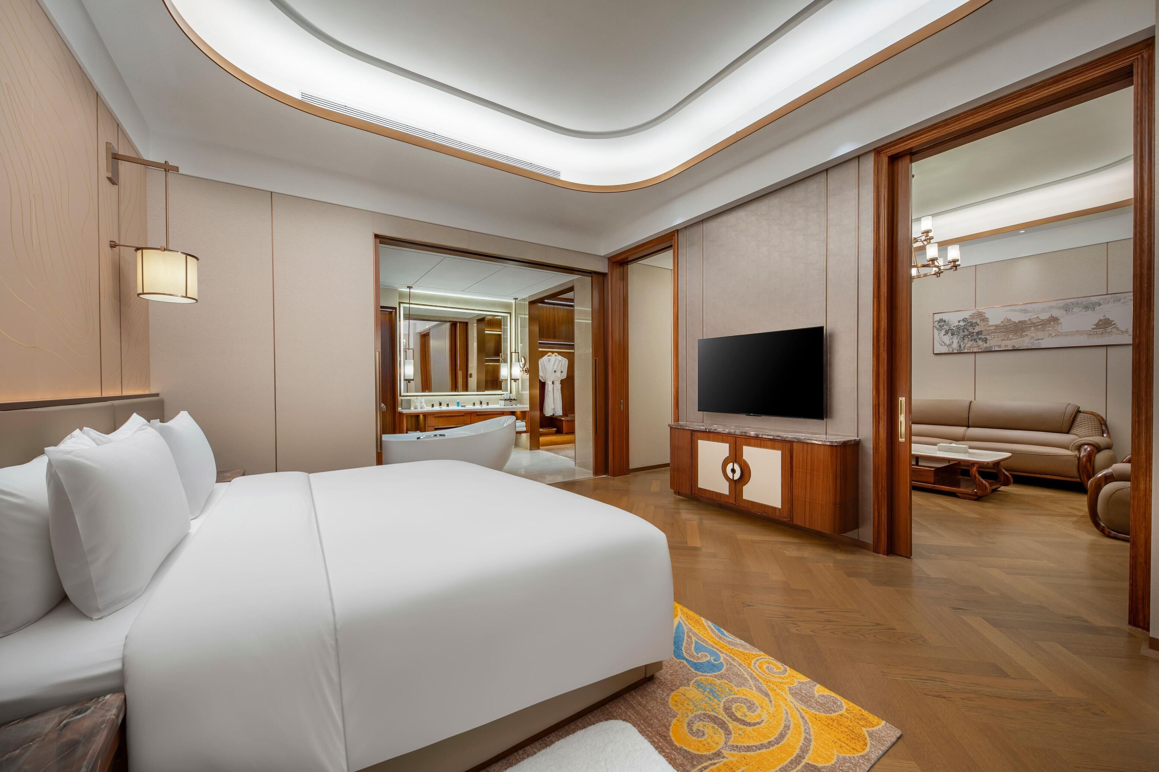 A hotel room with a large bed, a television, a bathroom with a bathtub, and a living area with a sofa and a coffee table.