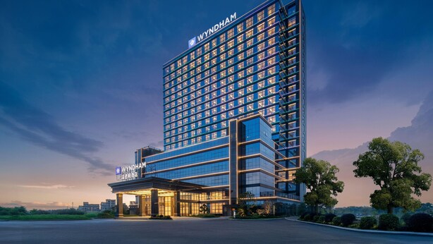 Un moderno edificio de hotel con un llamativo letrero 'WYNDHAM', que presenta una estructura de varios pisos con fachada de vidrio y una entrada bien iluminada.