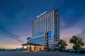 Un moderno edificio de hotel con un llamativo letrero 'WYNDHAM', que presenta una estructura de varios pisos con fachada de vidrio y una entrada bien iluminada.