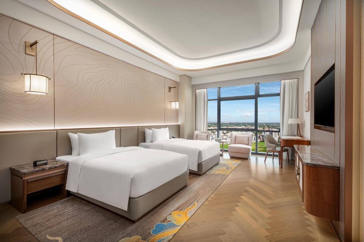 Una habitación de hotel moderna con dos camas, un escritorio, un televisor y vista a la ciudad.
