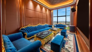 Una habitación lujosa con un amplio sofá azul, sillones con marcos dorados y una alfombra estampada.