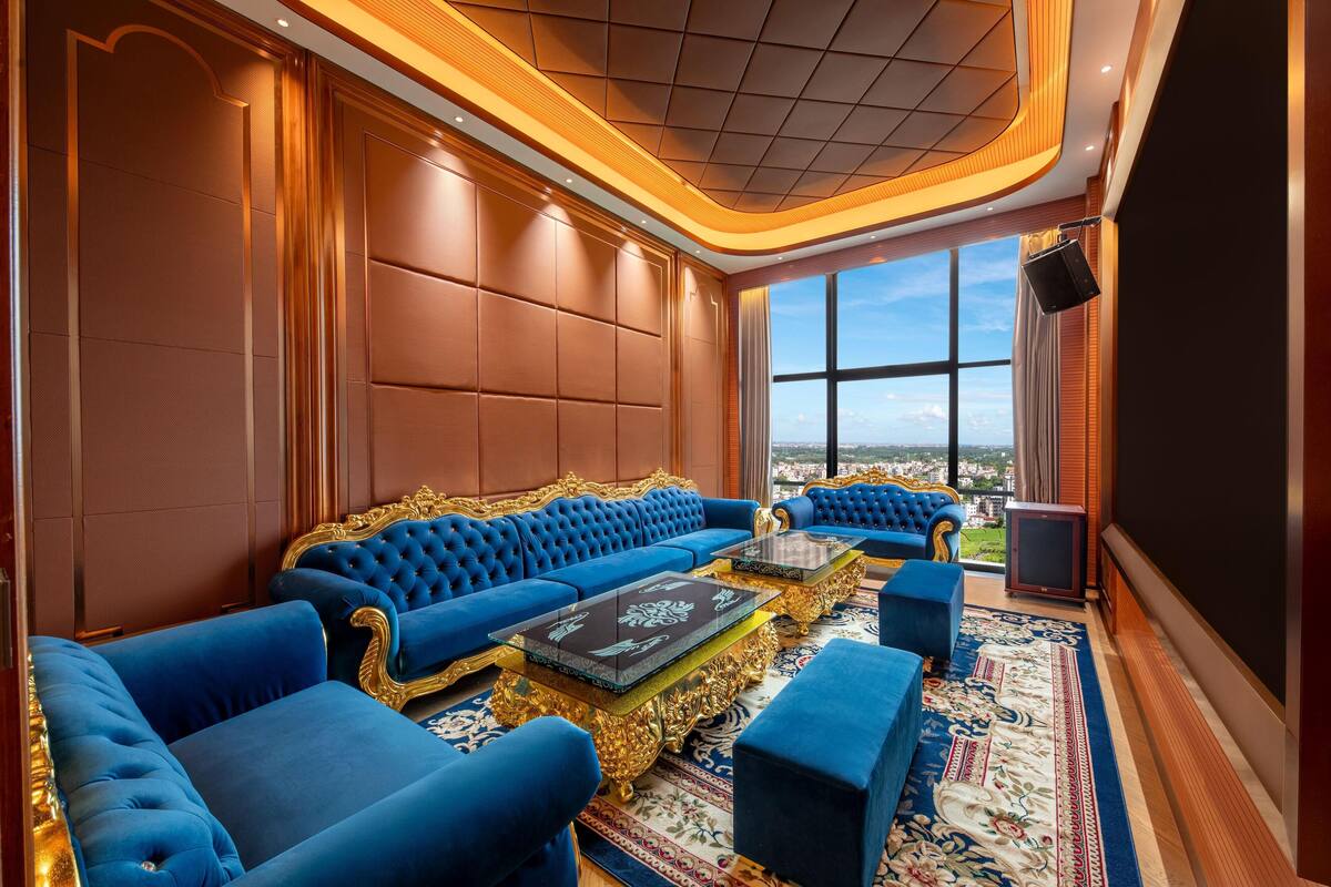 Una habitación lujosa con un amplio sofá azul, sillones con marcos dorados y una alfombra estampada.