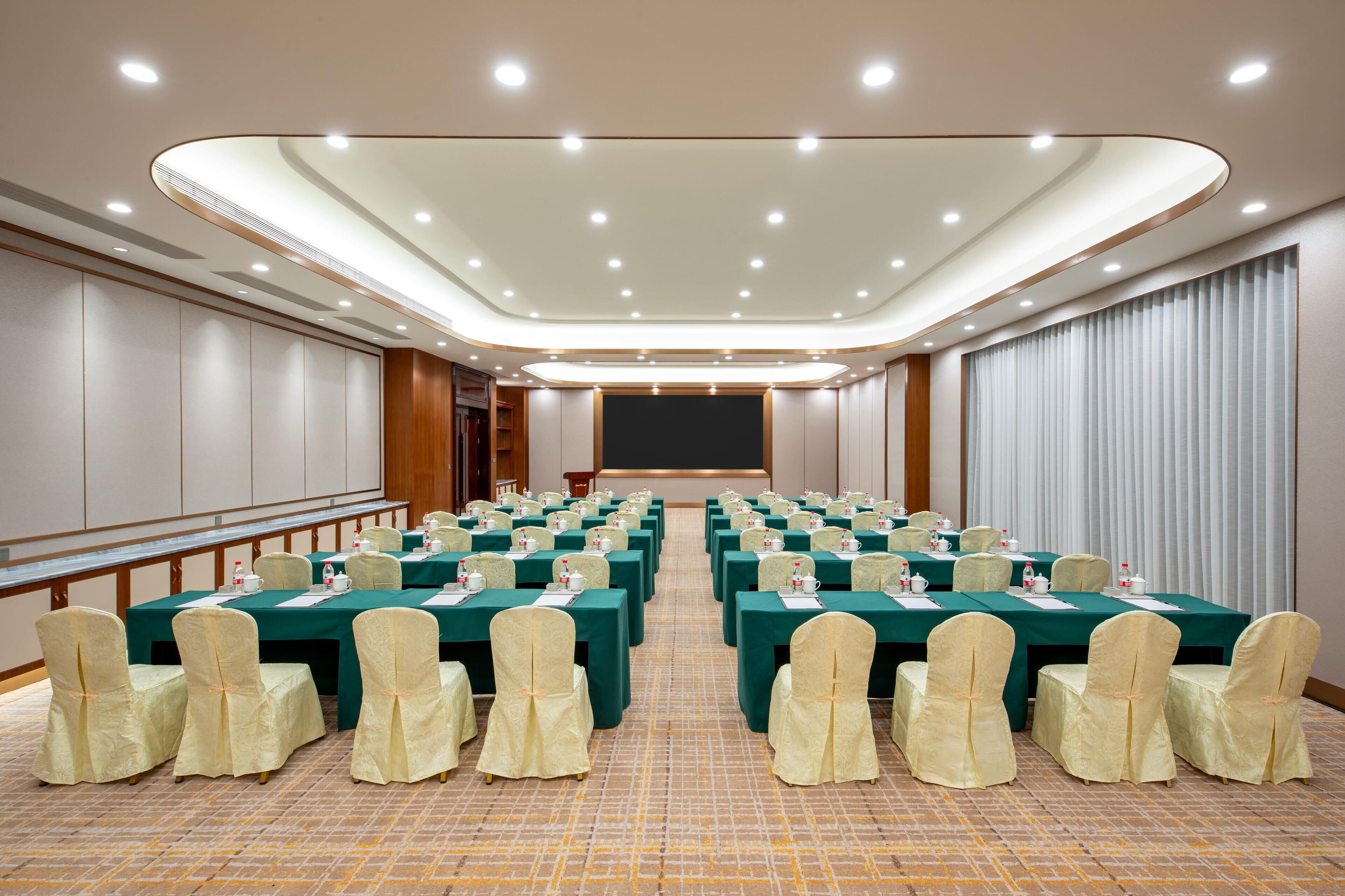 A conference room with rows of tables and chairs, a large screen, and a podium.