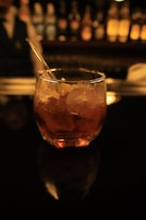Un vaso con pajita y cubitos de hielo sobre una superficie reflectante.