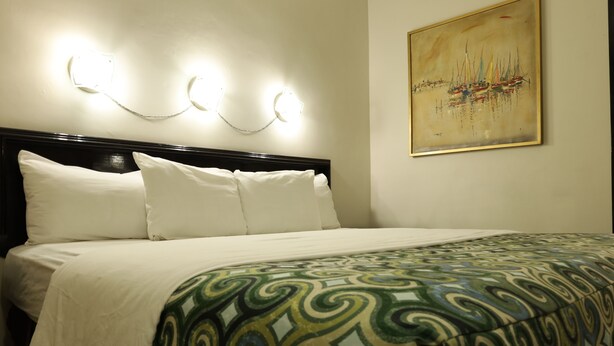 A hotel room with a bed, white pillows, a patterned bedspread, and a painting on the wall.