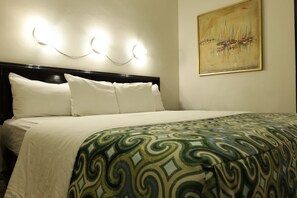 Una camera d'albergo con un letto, cuscini bianchi, una coperta a motivi e un quadro appeso al muro.