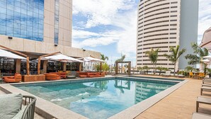 A pool area with lounge chairs and umbrellas, surrounded by tall buildings. - Horoh Grand Hotel (Cuiabá)