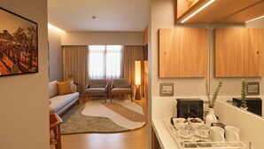 A modern living room with a sofa, two armchairs, a coffee table, and a dining area with a coffee machine and cups. - Horoh Grand Hotel (Cuiabá)