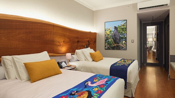 A hotel room with two beds, a wooden headboard, a painting of a bird, and a view into the hallway. - Horoh Grand Hotel (Cuiabá)