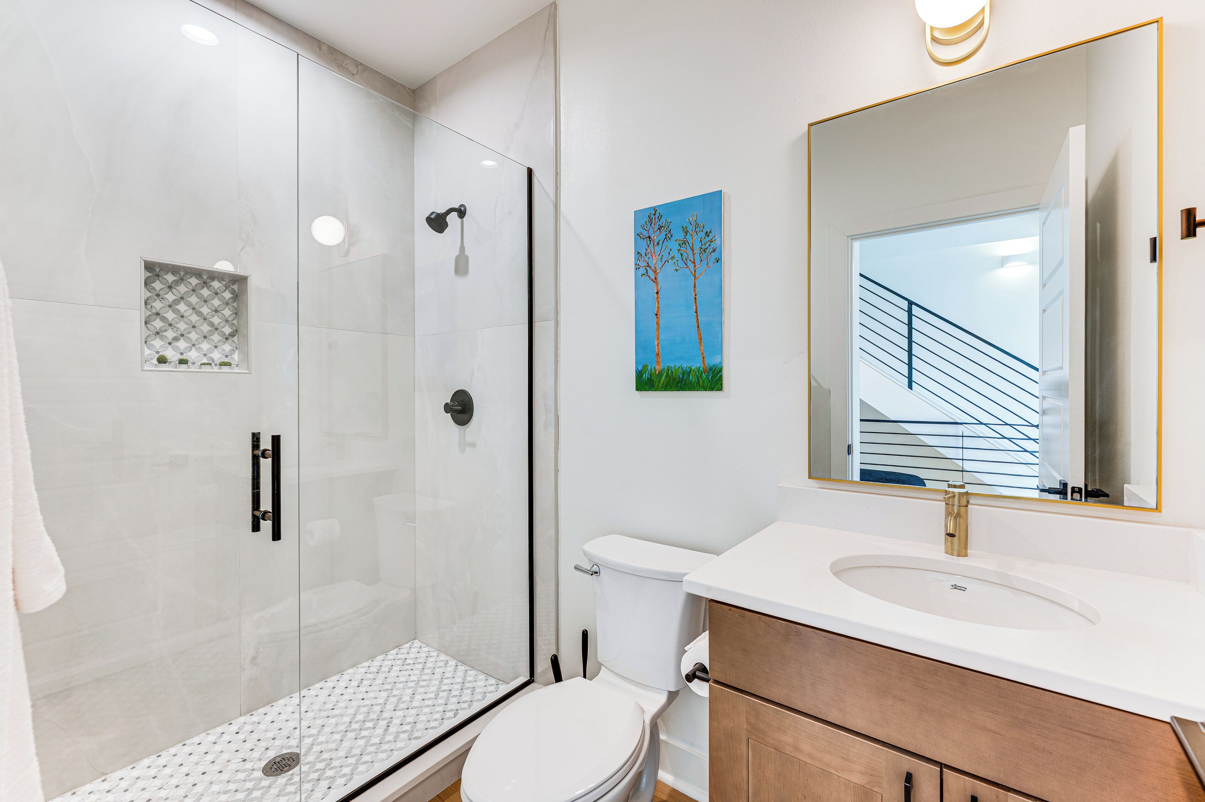 A modern bathroom with a glass-enclosed shower, a white toilet, and a vanity with a large mirror.