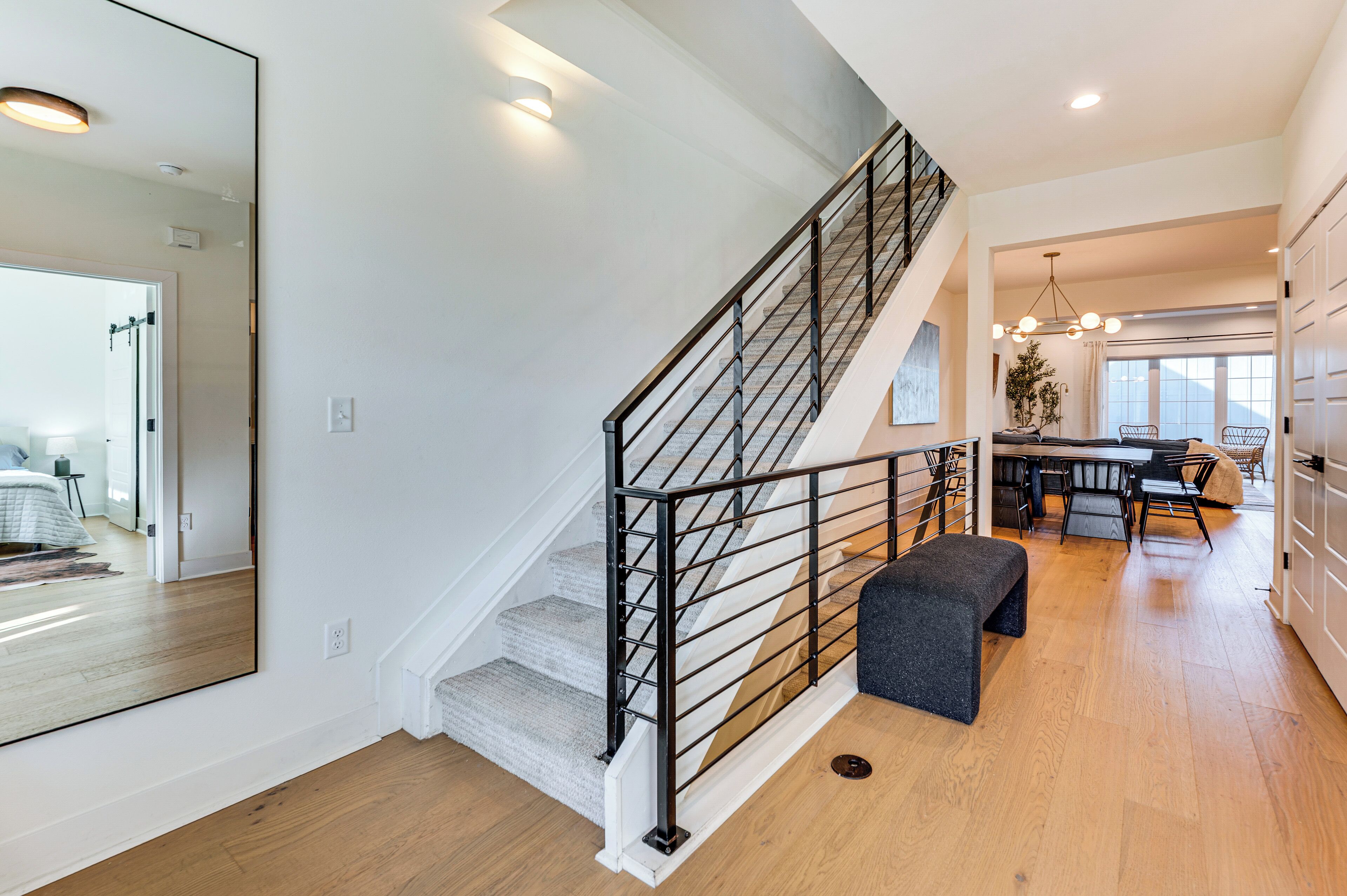 Un intérieur moderne avec un escalier, un coin repas et un grand miroir qui reflète une chambre à coucher.
