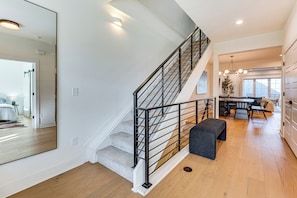 Un intérieur moderne avec un escalier, un plancher en bois, un coin repas et un grand miroir.