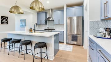 Une cuisine moderne dotée d’un îlot central, de tabourets de bar, d’appareils électroménagers en acier inoxydable et de luminaires suspendus.