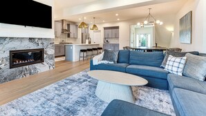 En moderne stue med pejs, en blå sofa og et spiseområde med et køkken i baggrunden.