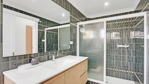 Une salle de bain moderne avec un grand miroir, deux vasques, un espace douche et un meuble-lavabo en bois.