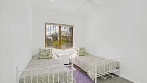 Une chambre avec deux lits simples, une fenêtre donnant sur l’extérieur et un ventilateur de plafond.